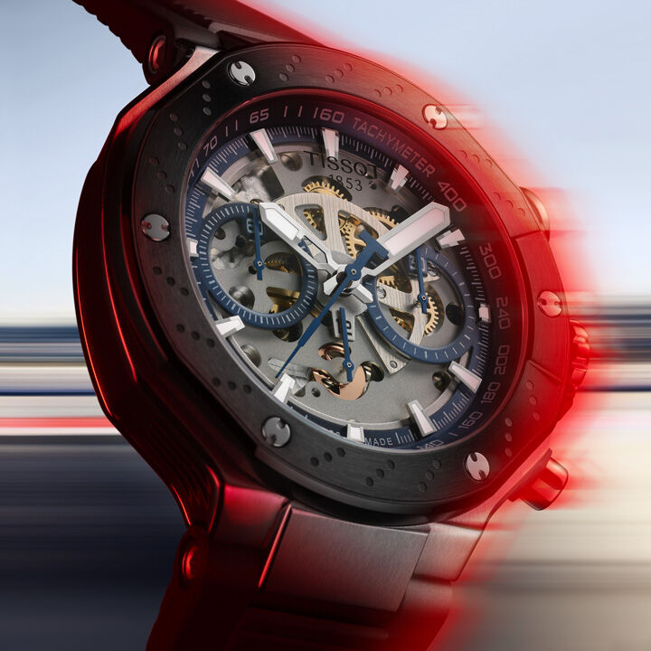 Tissot T-Race MotoGP 시계, 대담한 검은색 다이얼, 빨간색 액센트, 속도와 아드레날린을 불러일으키는 동적 모션 블러 배경.