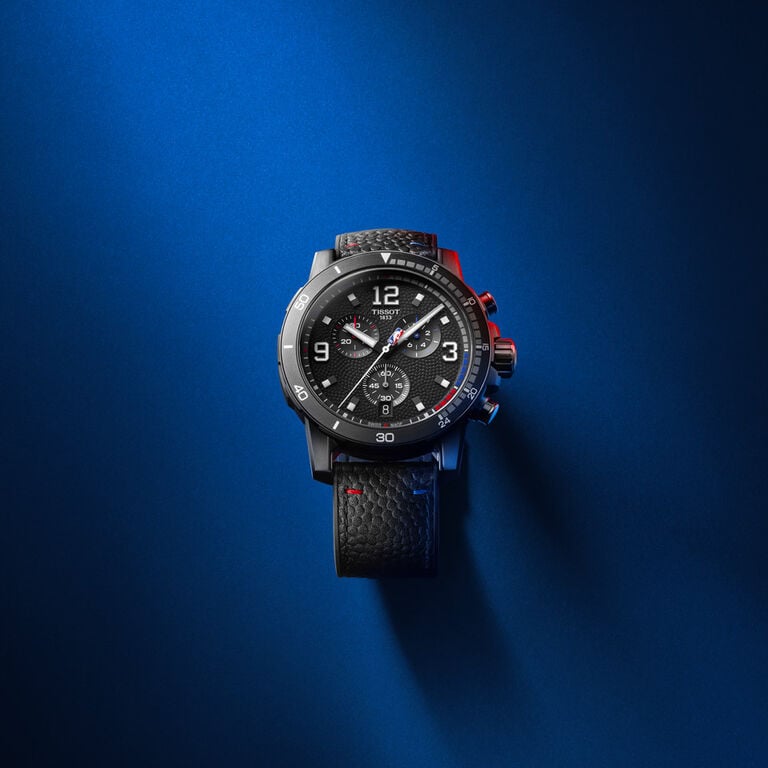 Tissot Supersport Chrono watch with a black textured dial, bold numerals, and a black leather strap with red stitching, set against a deep blue gradient background with dramatic lighting and shadows.